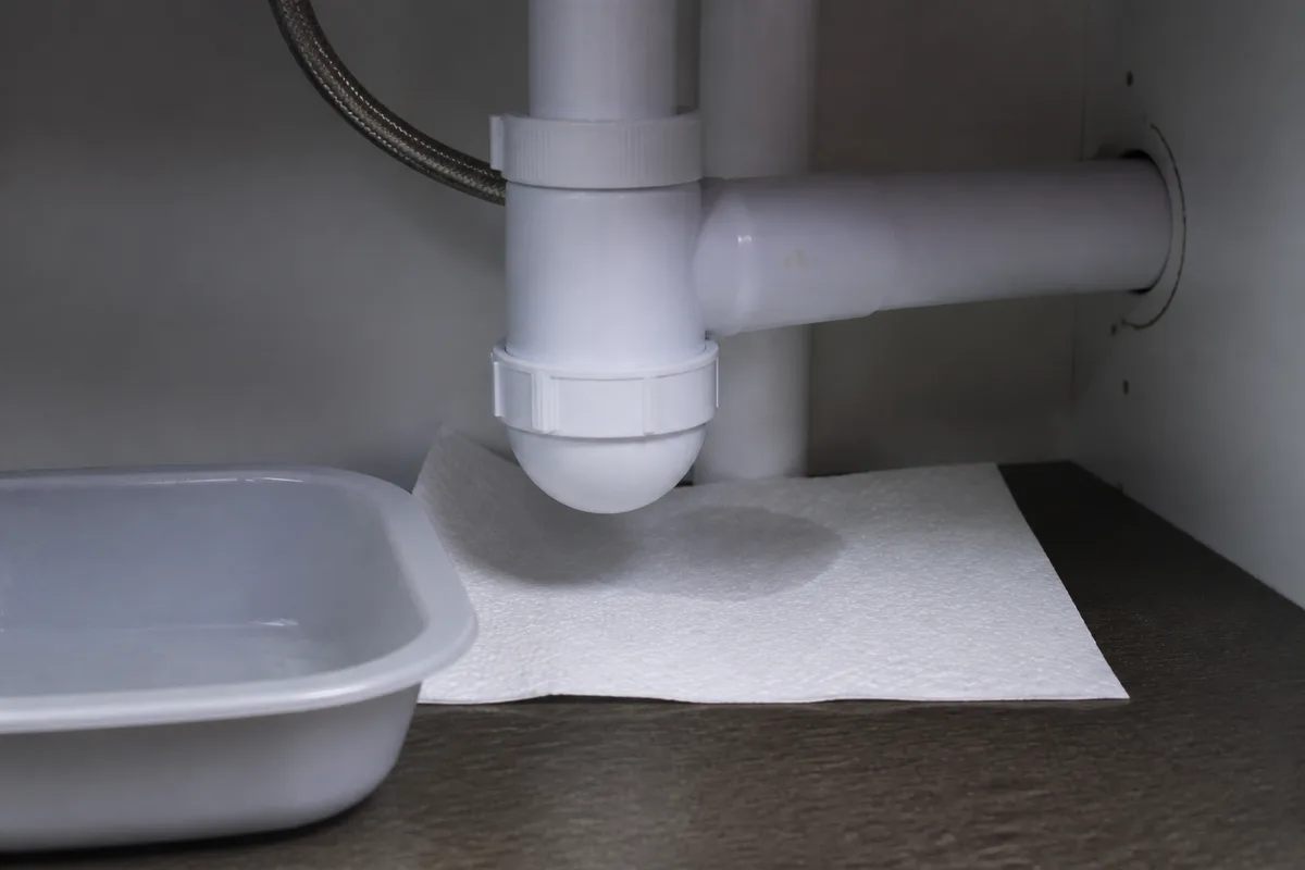 Feuille de papier absorbant posee sous les bagues d un siphon pour reperer une microfuite dans un meuble sous evier